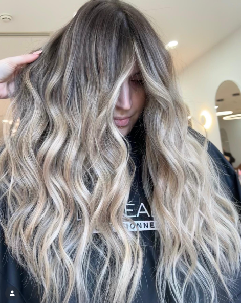 Creamy blonde hair with dark roots gives a stylish and modern contrast.