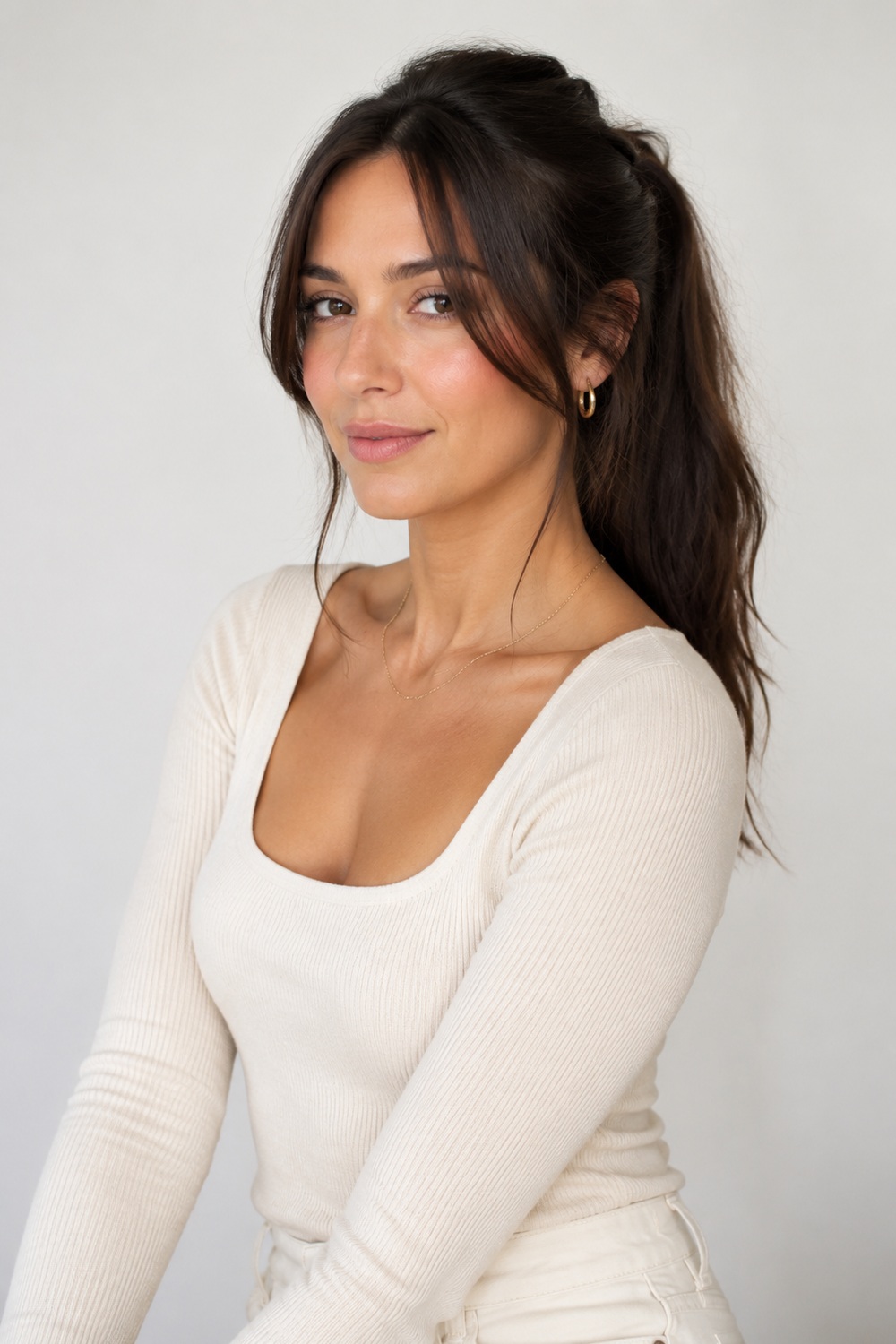 Long brunette hair styled in a soft high ponytail with loose curtain bangs framing the cheeks.