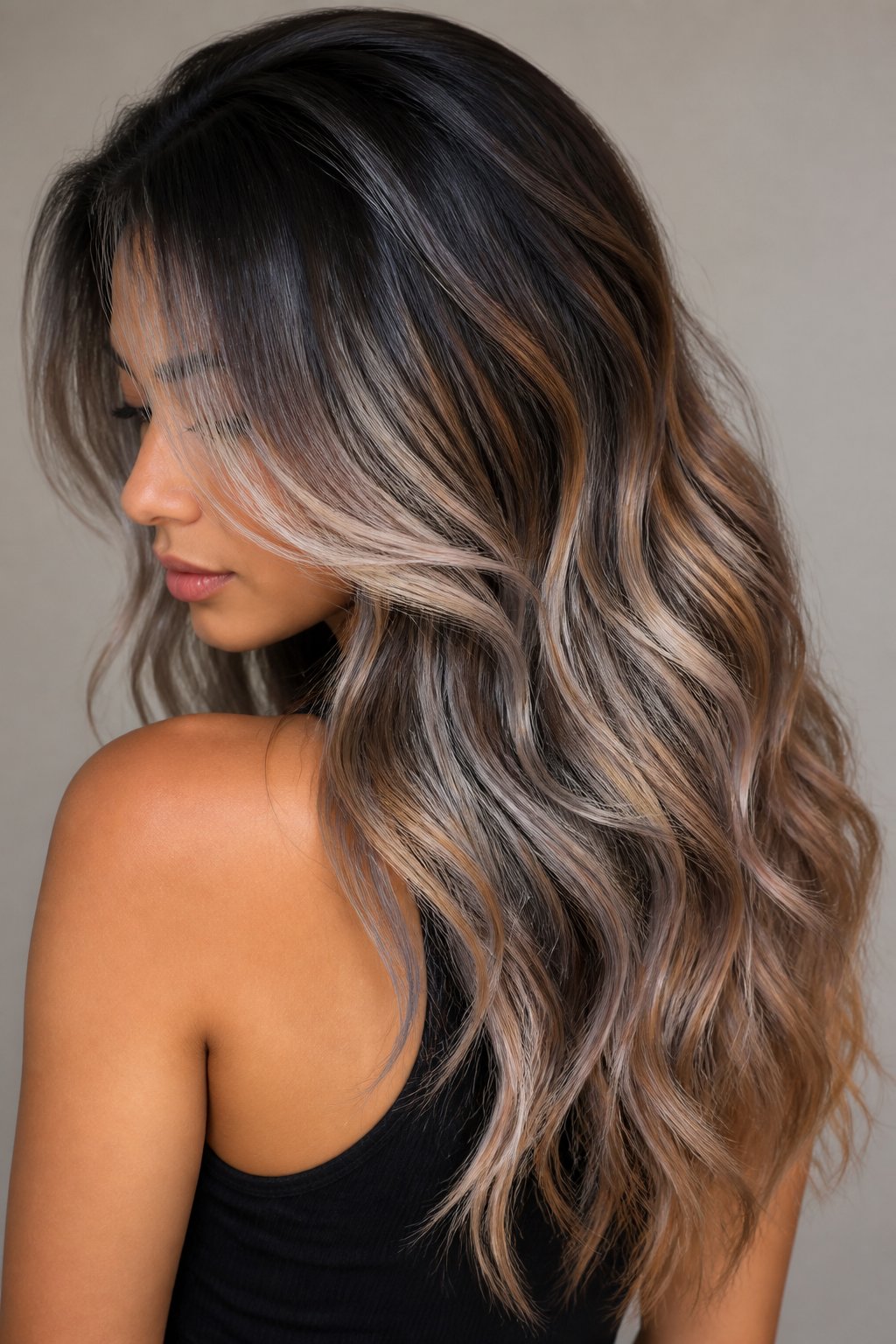 Long wavy smoky balayage with dark roots, ash-gray ribbons, and warm brown calico tones.